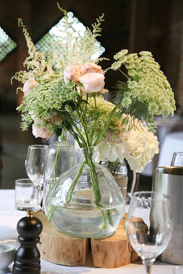 shustoke farm barns wedding flowers passion for flowers rustic centrepiece glass bottles vases on tree slice blush pink roses amni astilbe