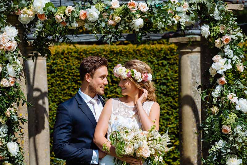 Stunning-flower-arch-for-outdoor-wedding-ceremony-at-Birtsmorton-Court-by-Passion-for-Flowers-bride-is-wearing-a-rose-flower-crown