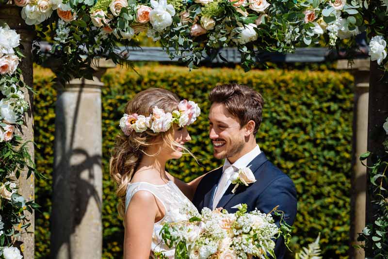 Stunning-flower-arch-for-outdoor-wedding-ceremony-at-Birtsmorton-Court-by-Passion-for-Flowers-bride-is-wearing-a-rose-flower-crown