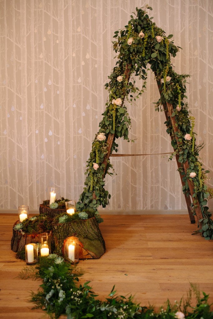 woodland rustic wedding ceremony with tree stumps candles moss arch for bride and groom to stand in front made from ladders