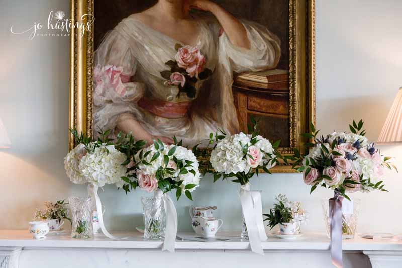 Bride and bridesmaids bouquets delivered by florist in glass vases set up on fireplace at Heath House