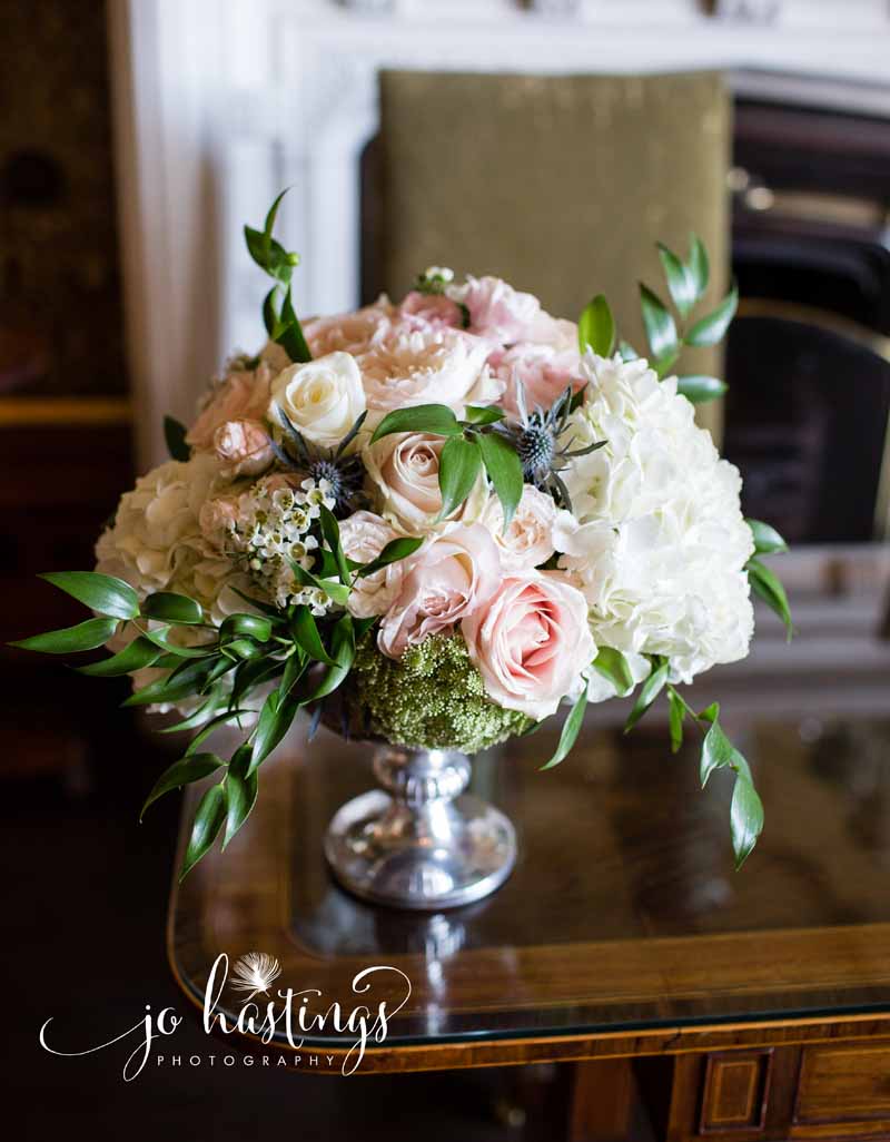 Footed silver bowl with dusky pink roses, dusty blue thistles and hydrangeas for ceremony floral arrangement at Heath House wedding