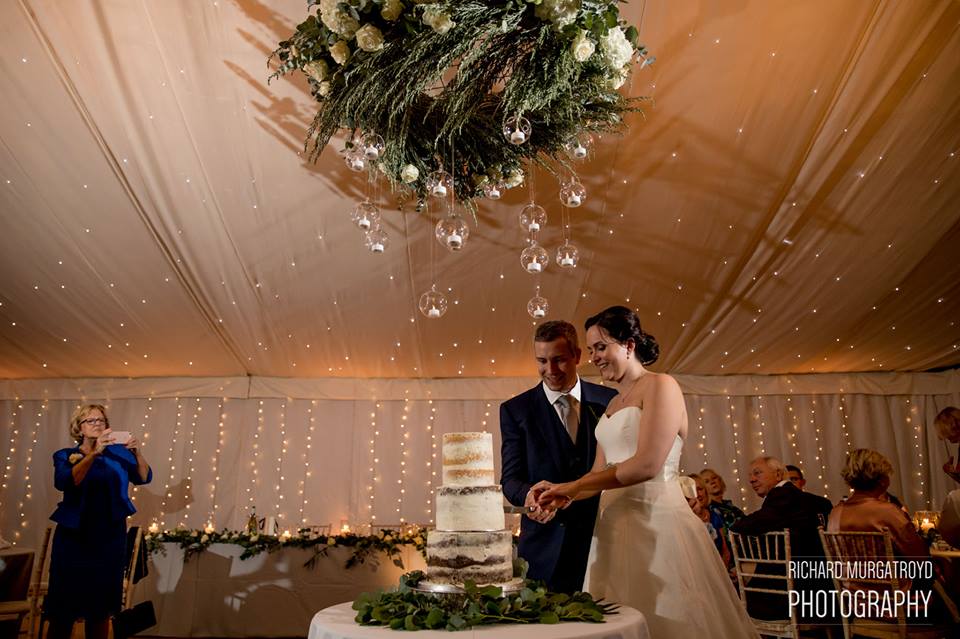 Amazing wedding cake flowers foliage around cake with hanging ring and candles above